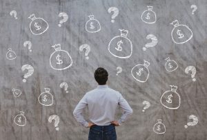 Man staring at a wall that has drawings of money and question marks