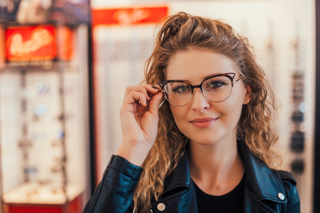 Image of a young attractive woman trying glasses at the optician - Healthy Vision Month eye exams